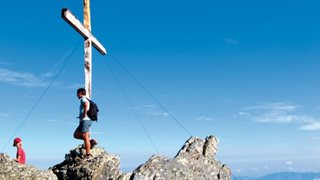 2 Wanderer auf dem Gipfelkreuz auf einem Berg in Korsika