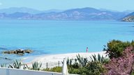 Eine junge Frau spaziert alleine an einem einsamen Strand auf Korsika