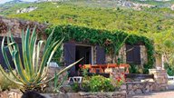 Ferienhaus und Terrasse aus Stein in der Natur mit viel Grün