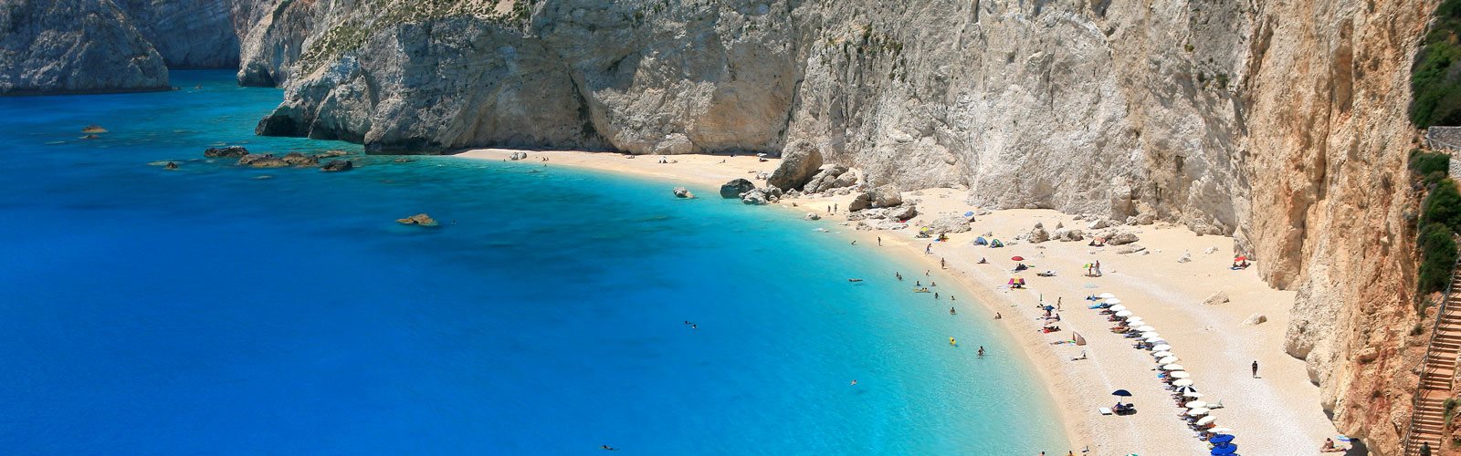 Wunderschöner griechischer Strand mit leuchtendem Meer neben steiler Küstenwand